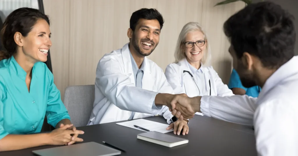 Young male PA shakes hands with his colleague across a conference table